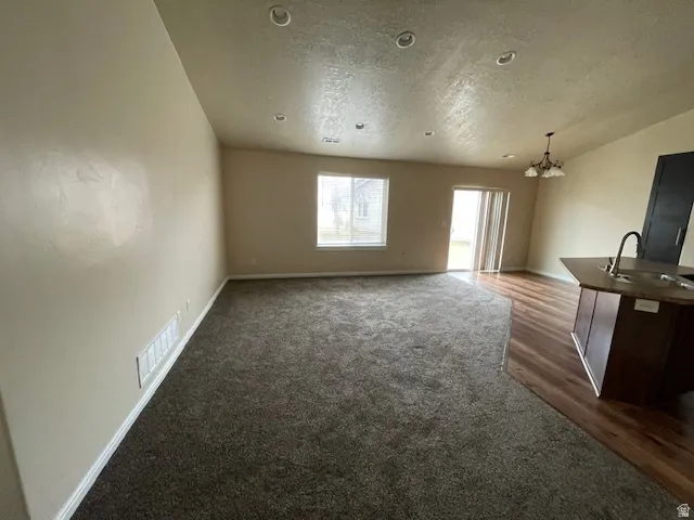 Unfurnished living room featuring a chandelier and dark carpet