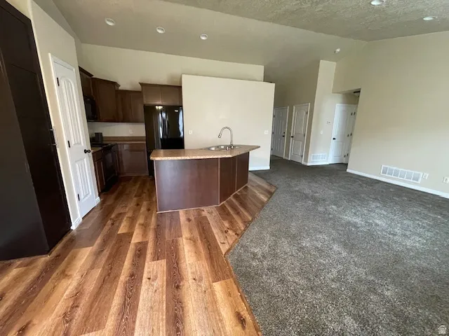 Kitchen with open floor plan, dark wood finish cabinetry, a kitchen island with sink, dark wood-style flooring, and a high textured ceiling