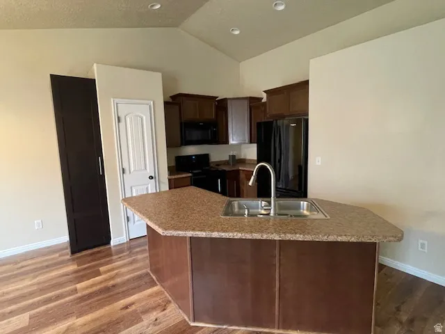 Kitchen with dark wood finish cabinets, black appliances, light countertops, dark wood-style flooring, and vaulted ceiling