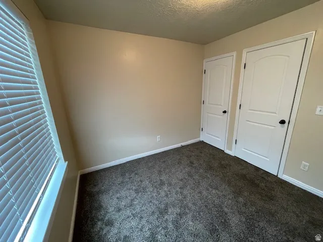 Unfurnished bedroom with dark carpet, a textured ceiling, and multiple windows