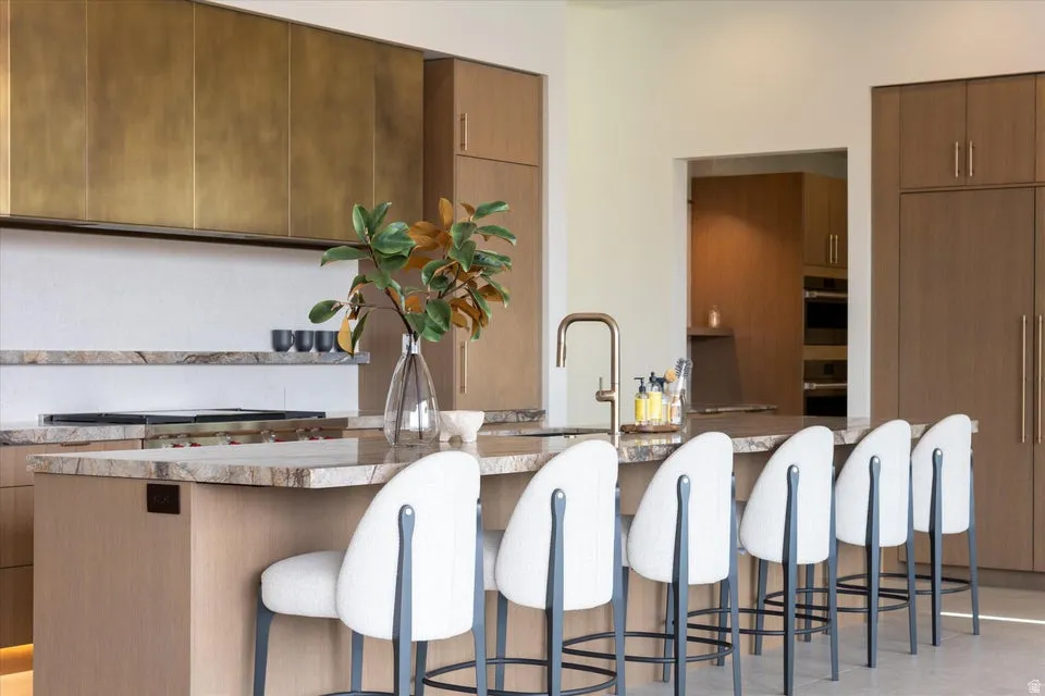 Kitchen with modern cabinets, a center island with sink, light stone counters, paneled built in fridge, and wood finish cabinetry