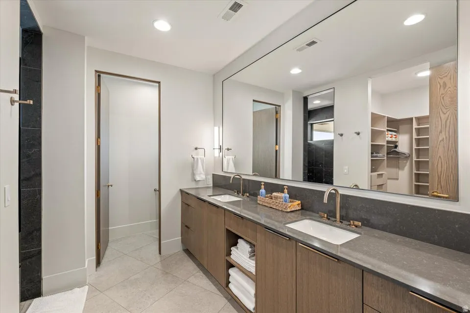 Full bathroom with double vanity, a walk in closet, light tile patterned floors, and recessed lighting