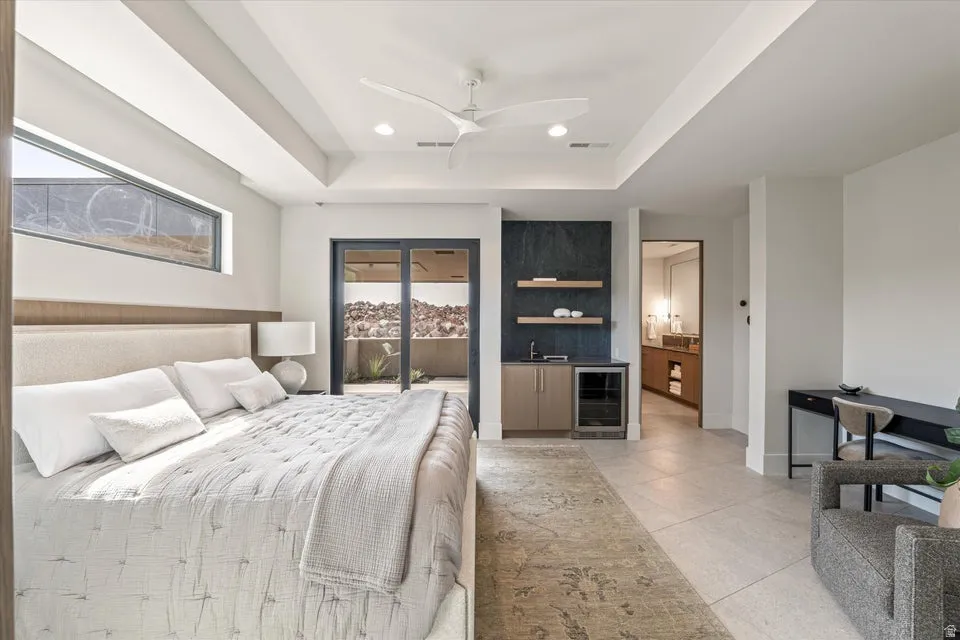 Bedroom with a raised ceiling, beverage cooler, bar with sink, recessed lighting, and ceiling fan