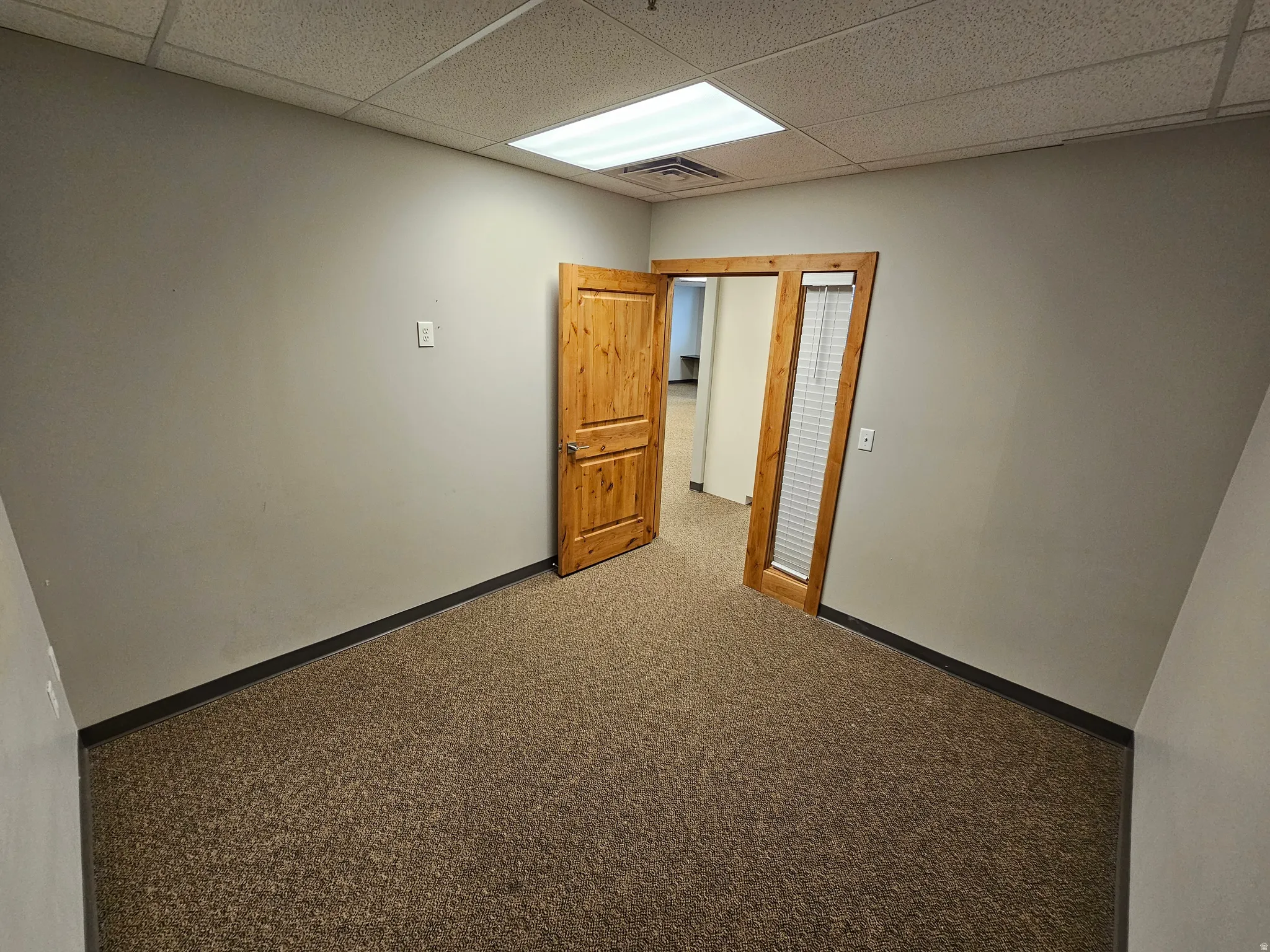 Carpeted empty room featuring a drop ceiling and baseboards
