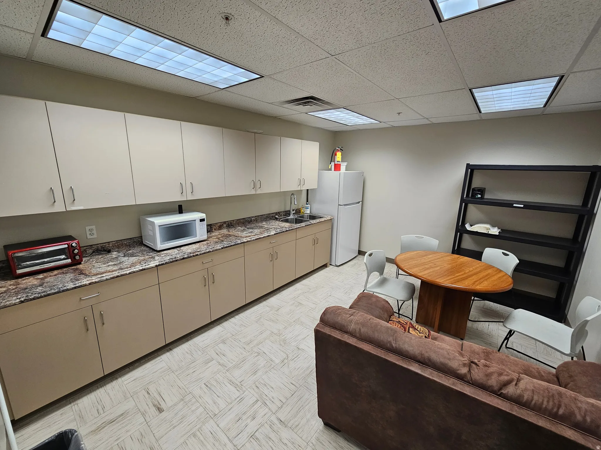 Kitchen with a drop ceiling, white appliances, light flooring, and dark stone counters
