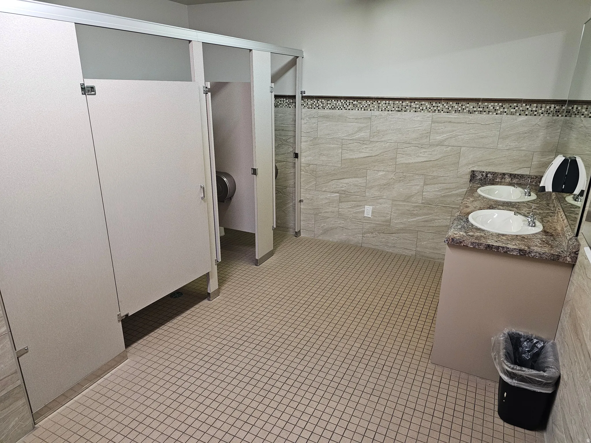 Bathroom featuring tile walls, wainscoting, double vanity, and light tile patterned floors
