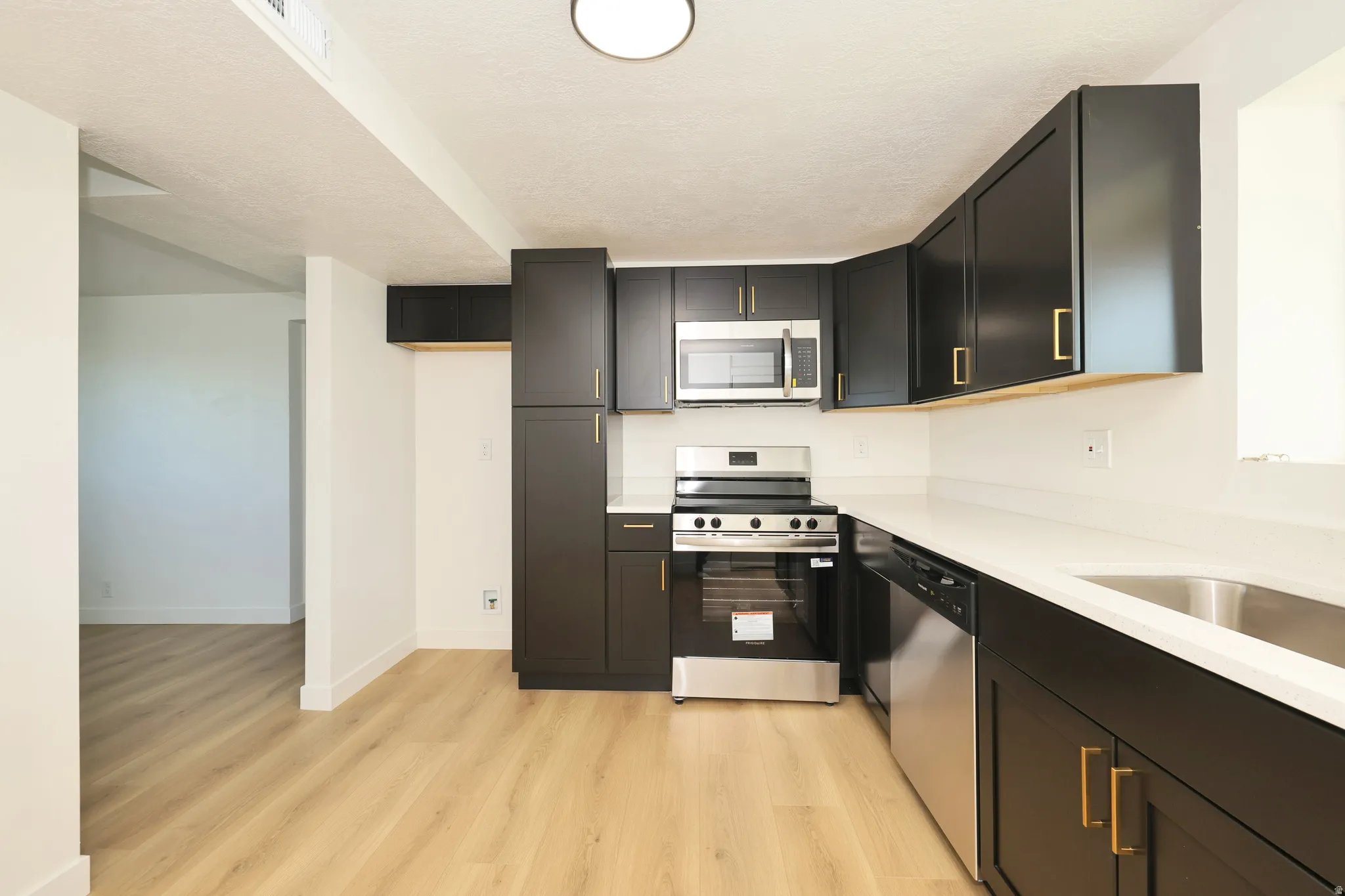 Kitchen with stainless steel appliances, dark cabinetry, light wood-style floors, and light stone countertops