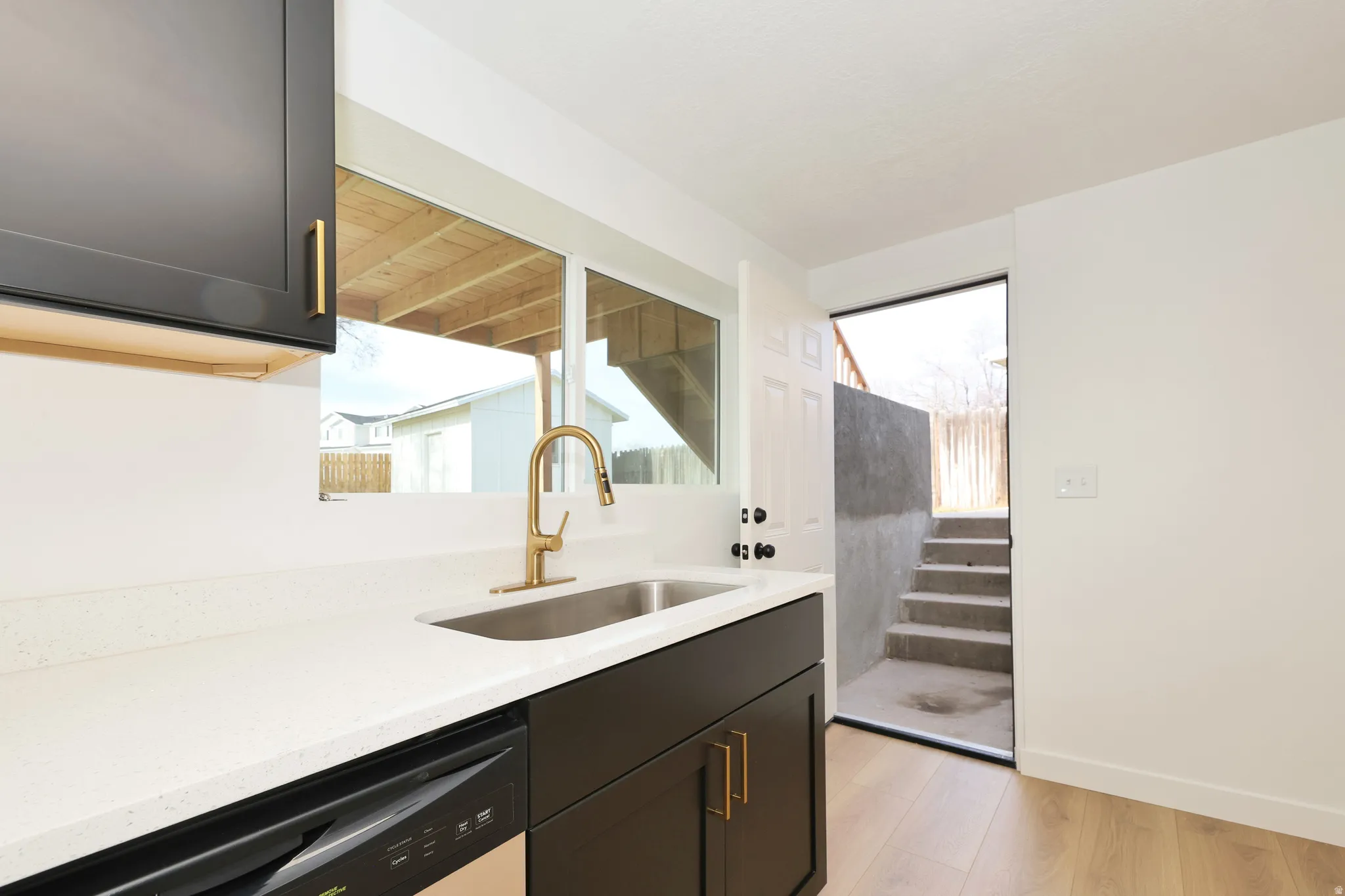 Kitchen featuring light wood finished floors, light stone countertops, stainless steel dishwasher, and plenty of natural light