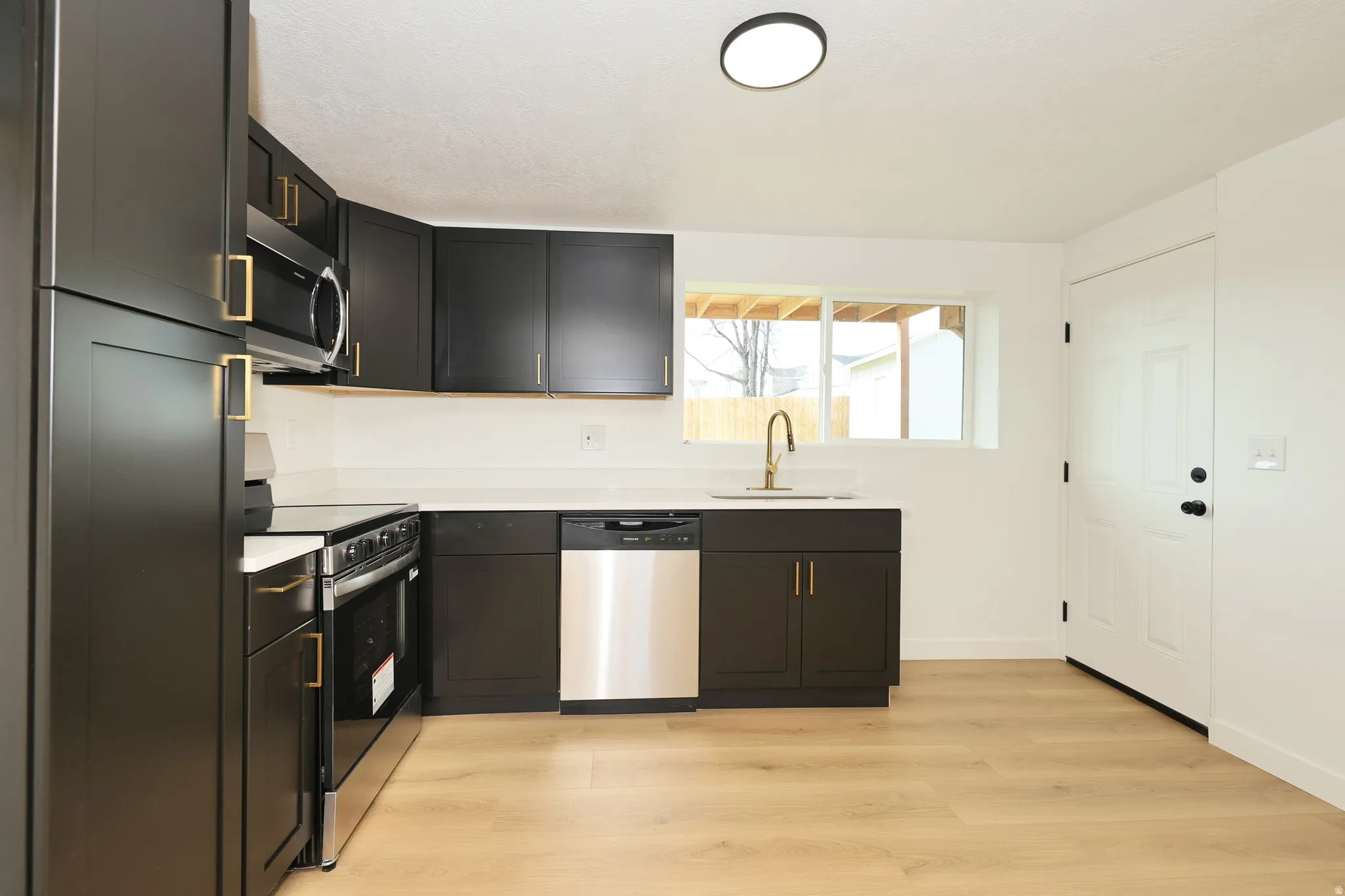 Kitchen featuring stainless steel appliances, light wood-style floors, and dark cabinets
