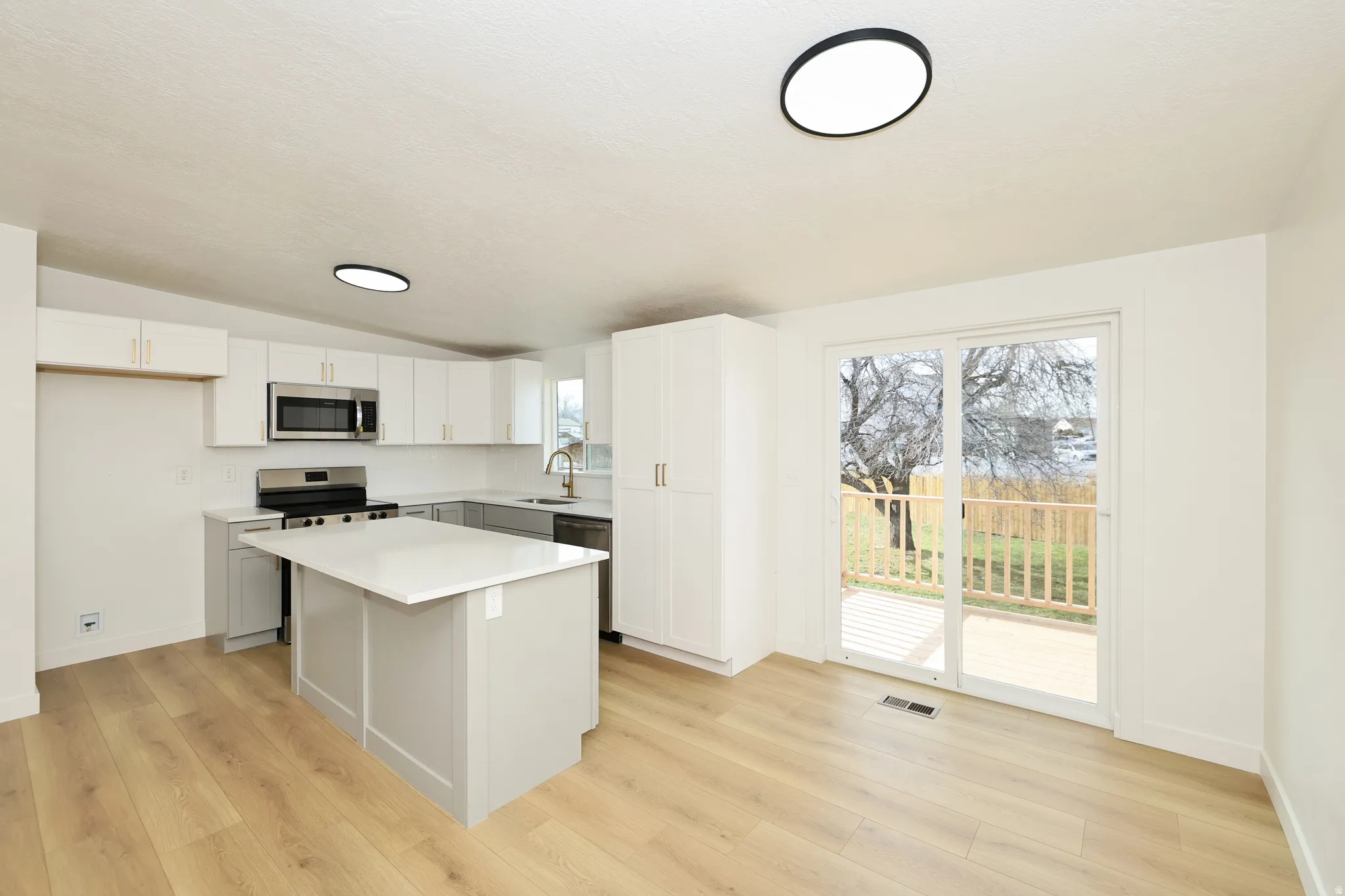 Kitchen with stainless steel appliances, vaulted ceiling, a kitchen island, white cabinetry, and light wood-style floors