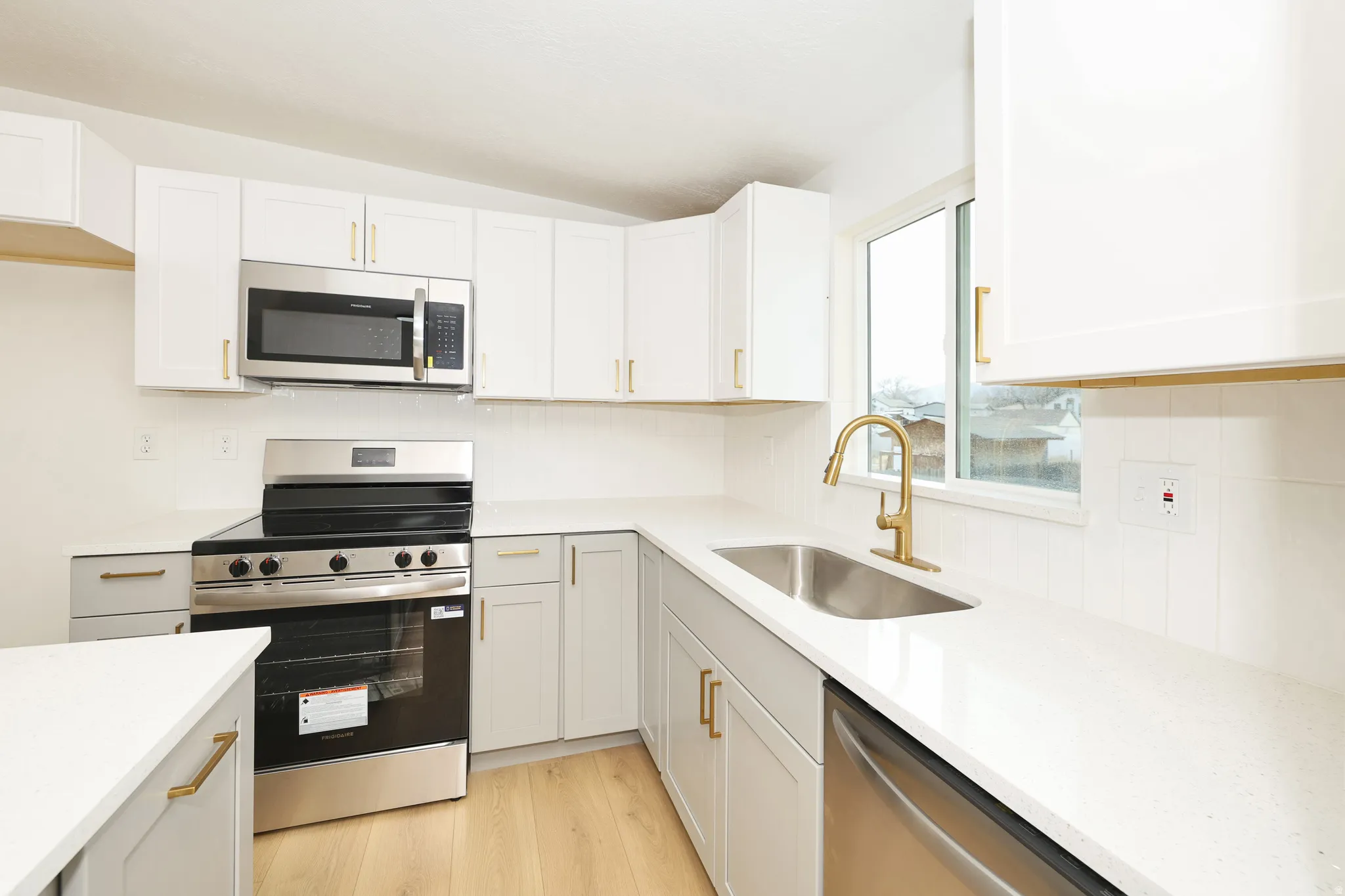Kitchen with stainless steel appliances, light wood finished floors, white cabinetry, and light stone countertops