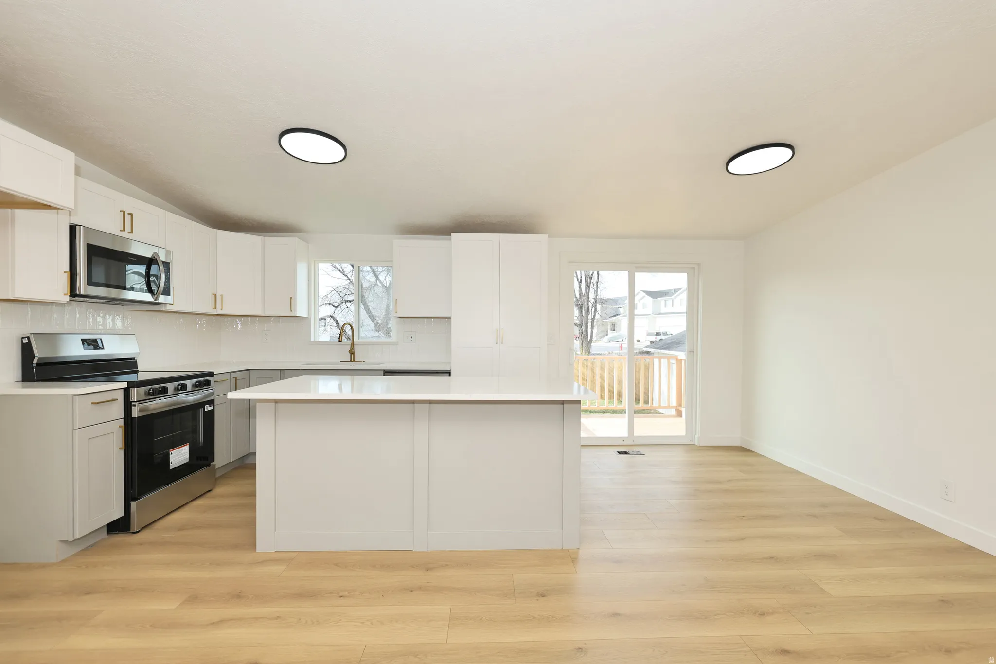 Kitchen featuring stainless steel appliances, light wood-type flooring, tasteful backsplash, a kitchen island, and white cabinets