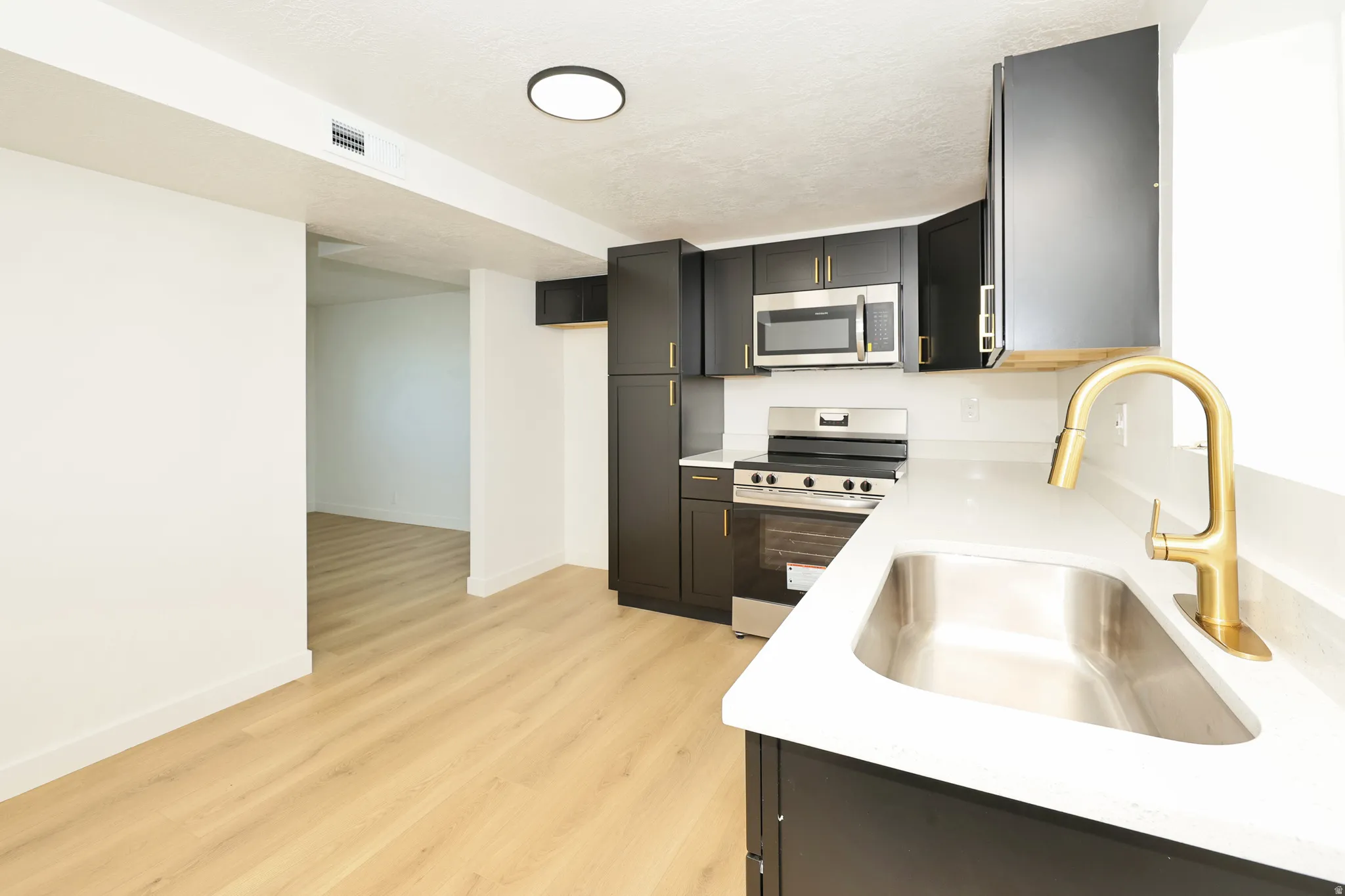 Kitchen with stainless steel appliances, light wood finished floors, light stone counters, and dark cabinetry