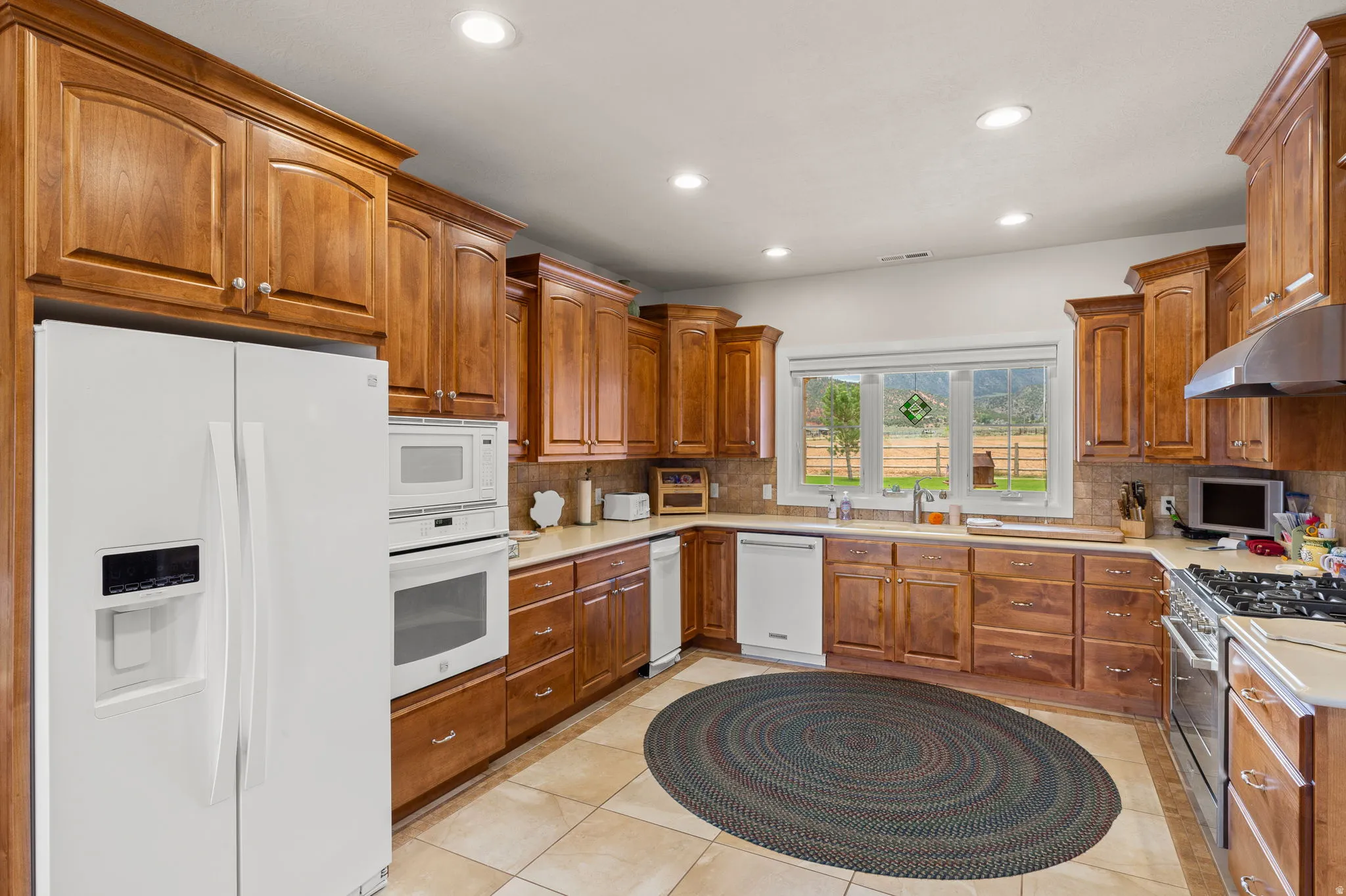 Kitchen with white appliances, wood finish cabinetry, light countertops, and recessed lighting