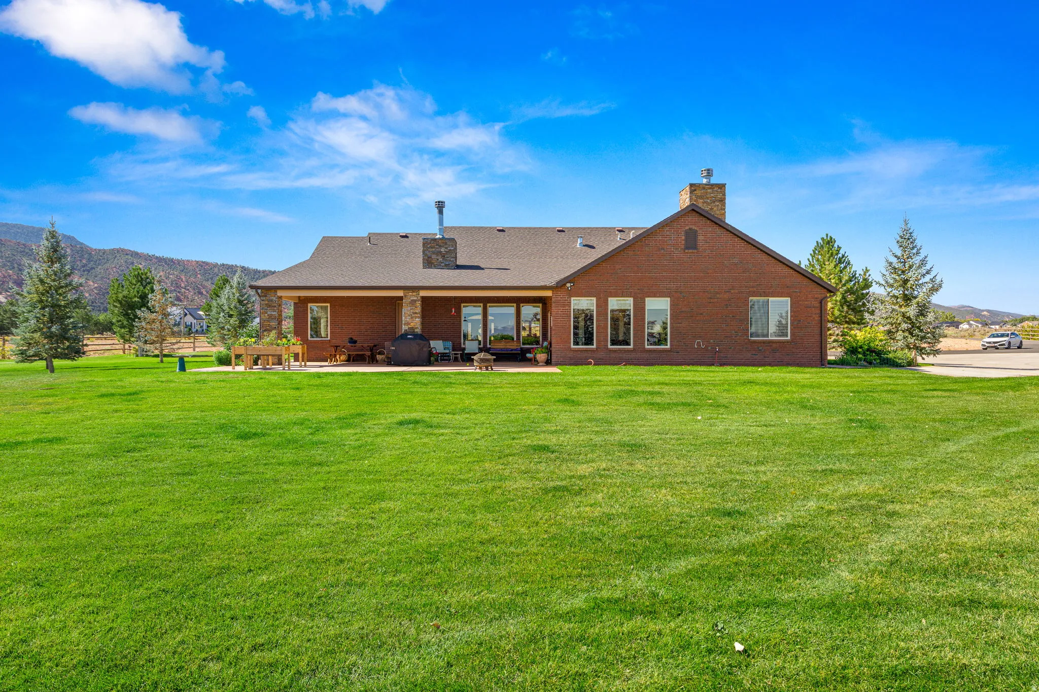 Back of property with a chimney, a mountain view, brick siding, a lawn, and a patio area