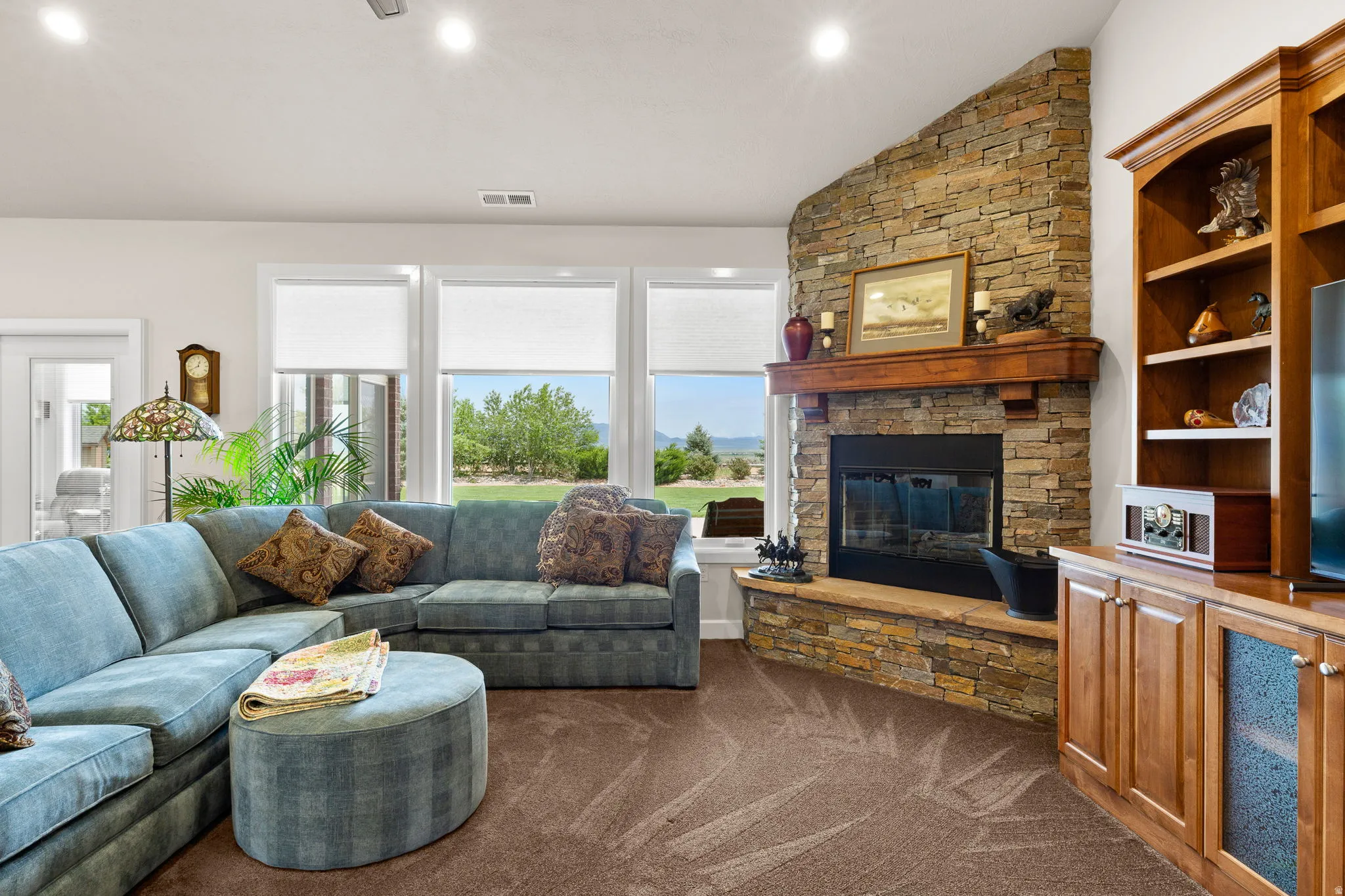 Living area featuring lofted ceiling, dark colored carpet, a stone fireplace, and recessed lighting