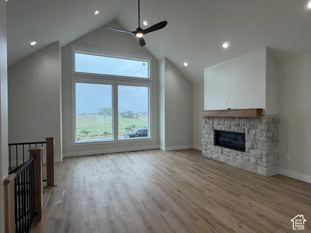 Spacious living area featuring a vaulted ceiling with recessed lighting, large windows, wood-finish flooring, a stone fireplace with a substantial wood mantle, and a ceiling fan