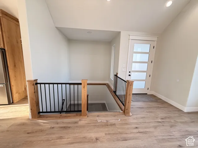 Wood-finish flooring, staircase with natural wood newel posts and black metal balusters, and a contemporary entryway door with frosted glass panels