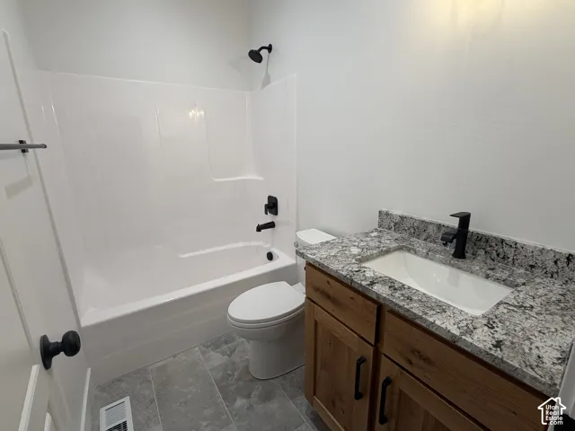 Bathroom featuring a white tub-shower combination, a vanity with wood-finish cabinetry, a white basin, a speckled countertop, and dark-finish fixtures