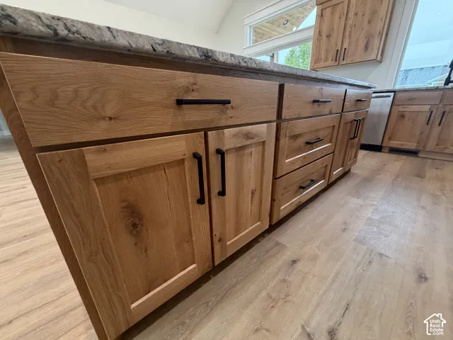 Kitchen island featuring a natural wood-finish cabinetry, black hardware, a light-toned countertop, and wood-finish flooring