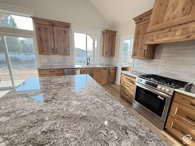 Gourmet kitchen featuring a large island with a stone countertop, wood-finish cabinetry, stainless steel range, and a tile backsplash