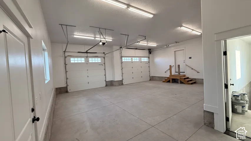 Spacious garage with concrete flooring, two overhead doors featuring frosted glass panels, and abundant ceiling-mounted strip lighting
