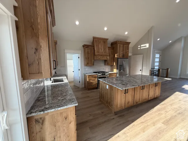 Kitchen featuring wood cabinetry, a large kitchen island with a stone countertop, stainless steel appliances, and wood-finish flooring