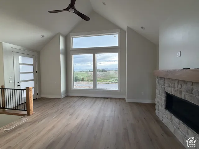 Spacious room featuring vaulted ceilings with a modern ceiling fan, wood-finish flooring, and a stone fireplace with a wood mantle