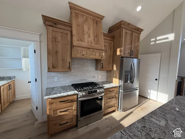 Stainless steel appliances, wood-finish cabinetry, gray speckled countertops, white subway tile backsplash, and wood-finish flooring