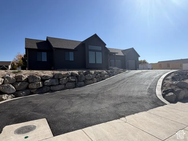 Contemporary exterior with dark horizontal siding, multiple gables, large windows, an integrated two-car garage, and a paved driveway with a stone retaining wall