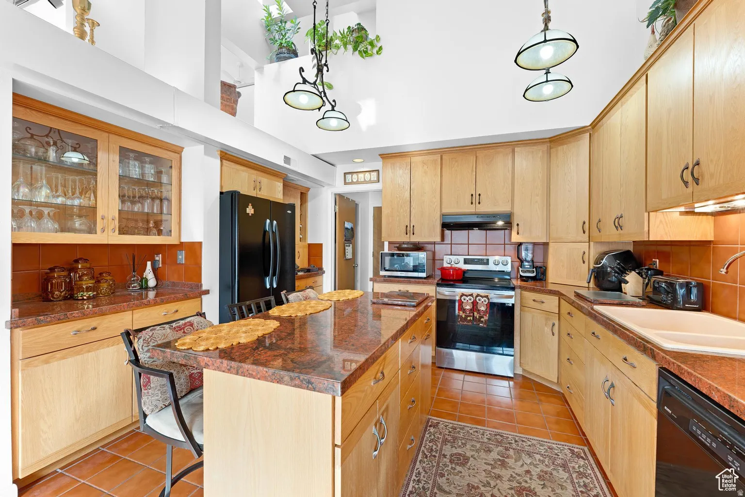 Kitchen with black appliances, decorative backsplash, a center island, a breakfast bar area, and a high ceiling