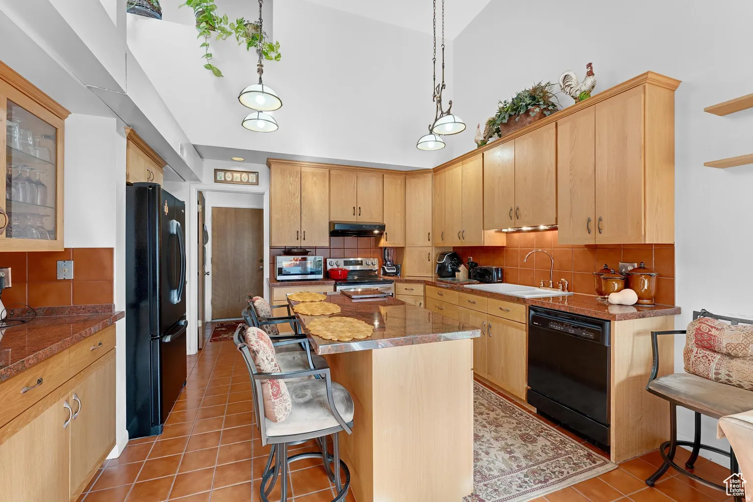 Kitchen featuring tasteful backsplash, black appliances, a center island, hanging light fixtures, and light wood finish cabinetry