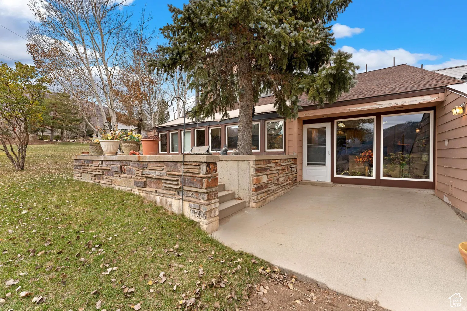 Rear view of house with a patio area, a lawn, stone siding, and a shingled roof