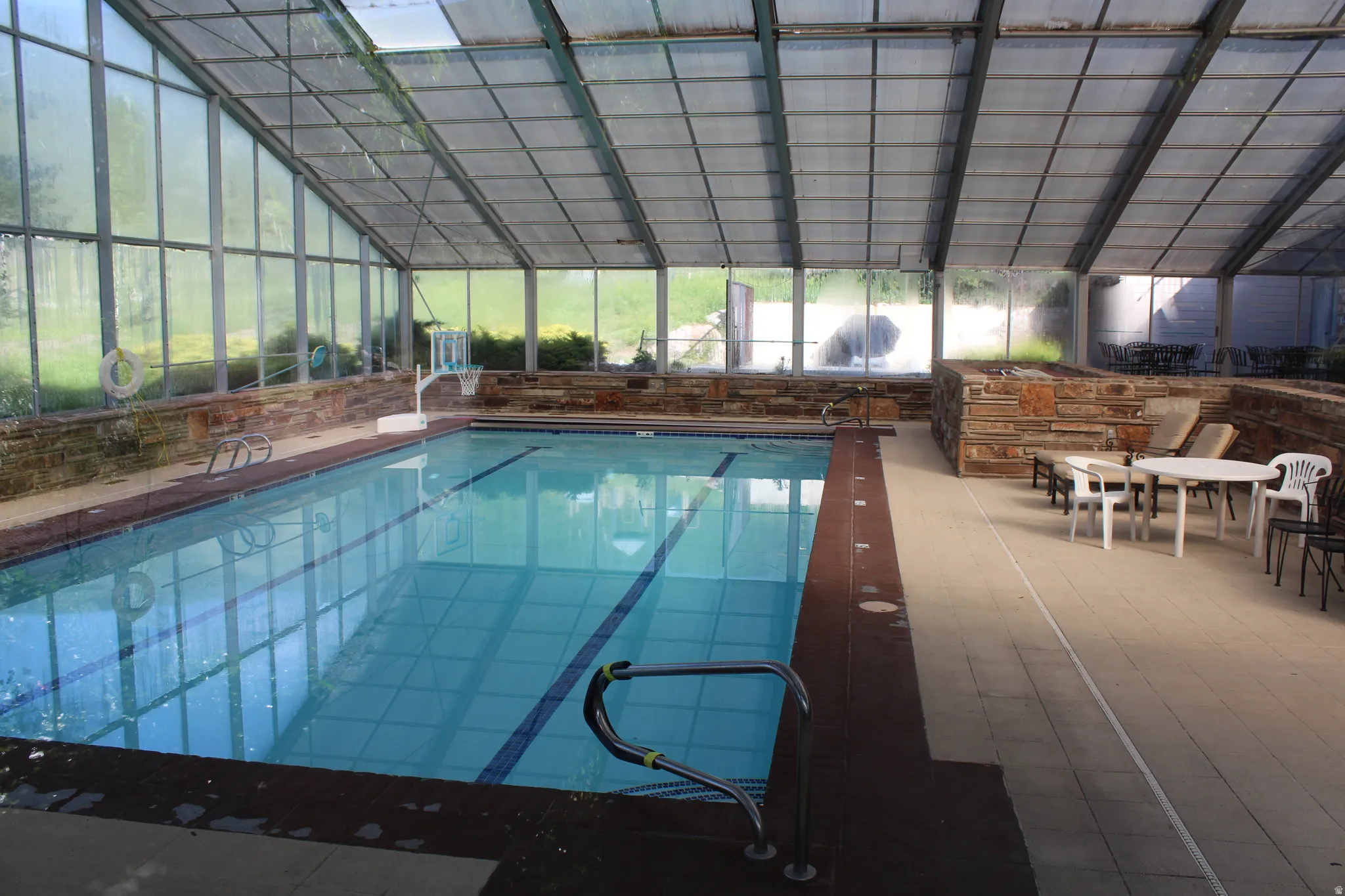 Indoor swimming pool featuring a full enclosure with transparent panels, a durable dark-toned pool surround, and light-toned floor tiling