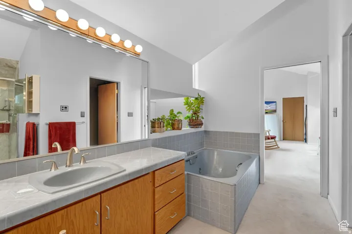 Bathroom featuring lofted ceiling, light colored carpet, vanity, a garden tub, and a shower