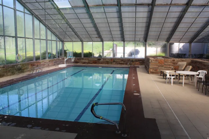 Indoor swimming pool featuring a full enclosure with transparent panels, a durable dark-toned pool surround, and light-toned floor tiling