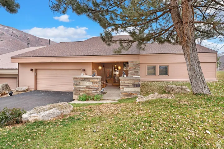 View of front of property featuring roof with shingles, a front yard, asphalt driveway, a garage, and stone siding