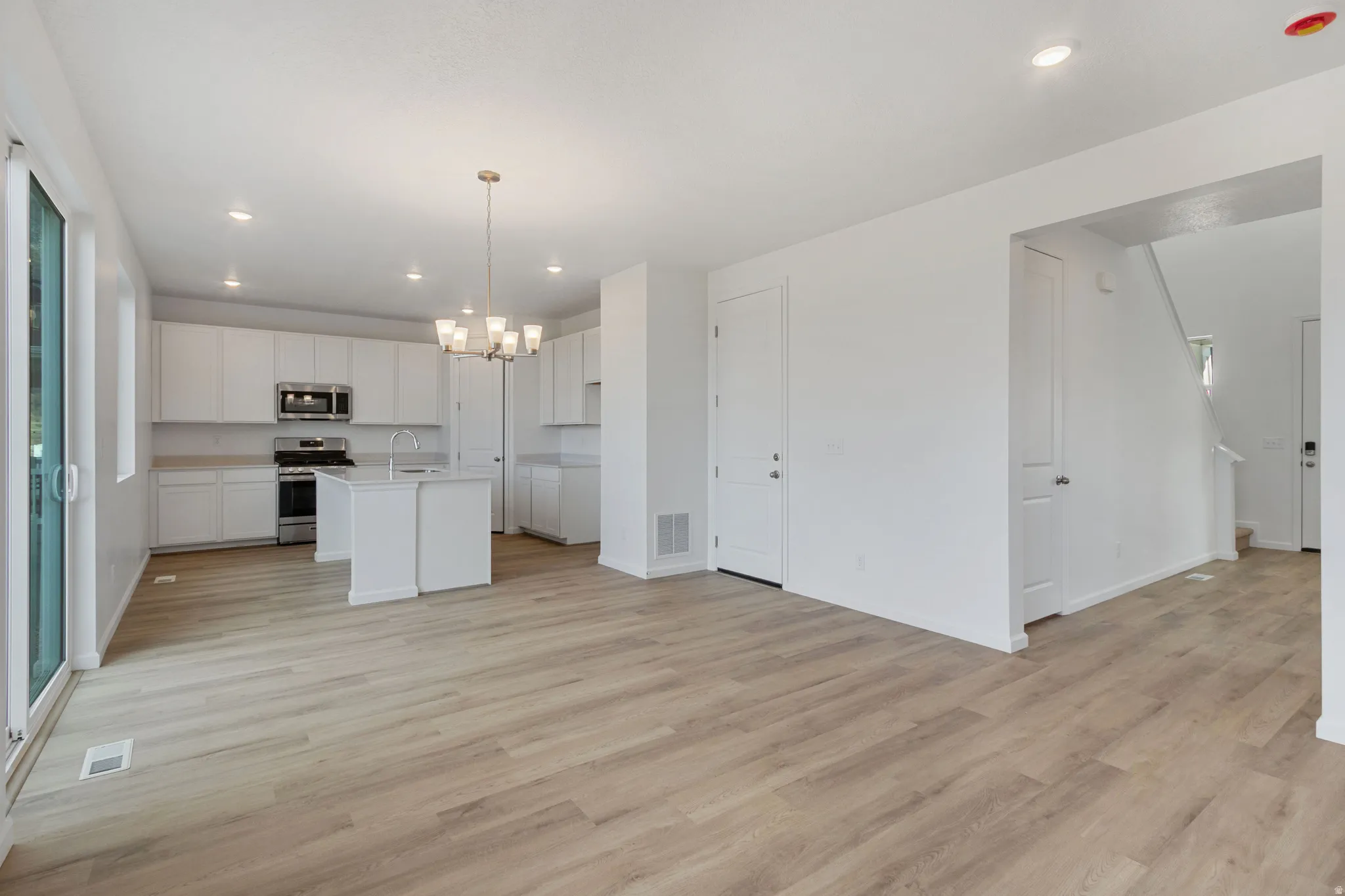 Kitchen featuring white cabinets, suspended lighting, stainless steel appliances, and open floor plan