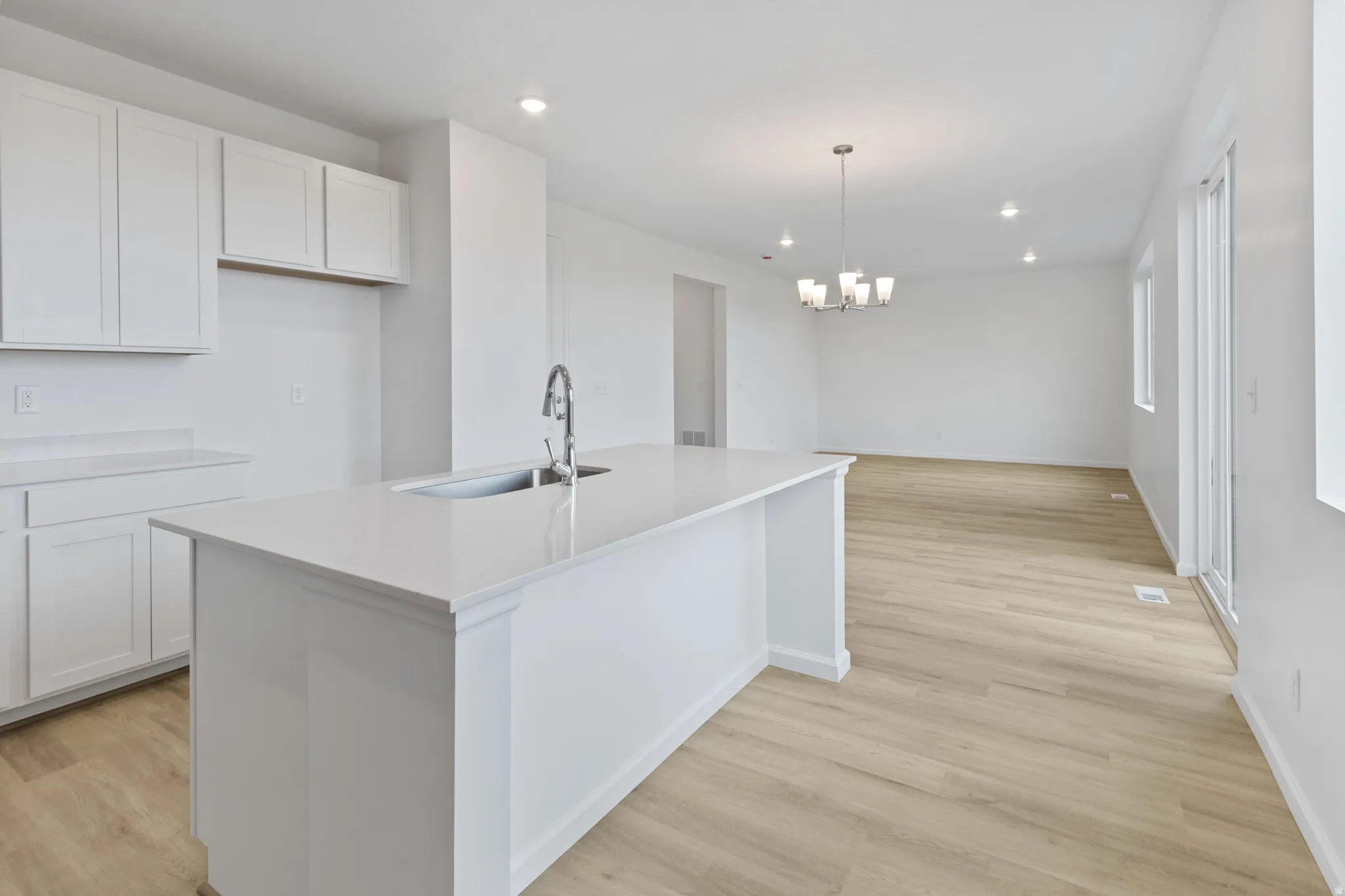 Kitchen with light wood-type flooring, an island with sink, light stone counters, white cabinets, and hanging lights