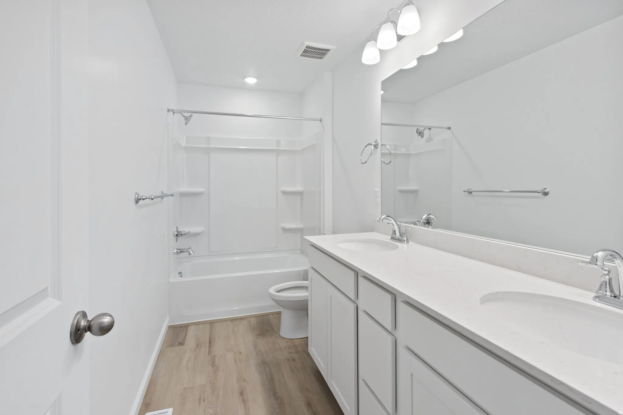 Bathroom with double vanity, light wood finished floors, and washtub / shower combination