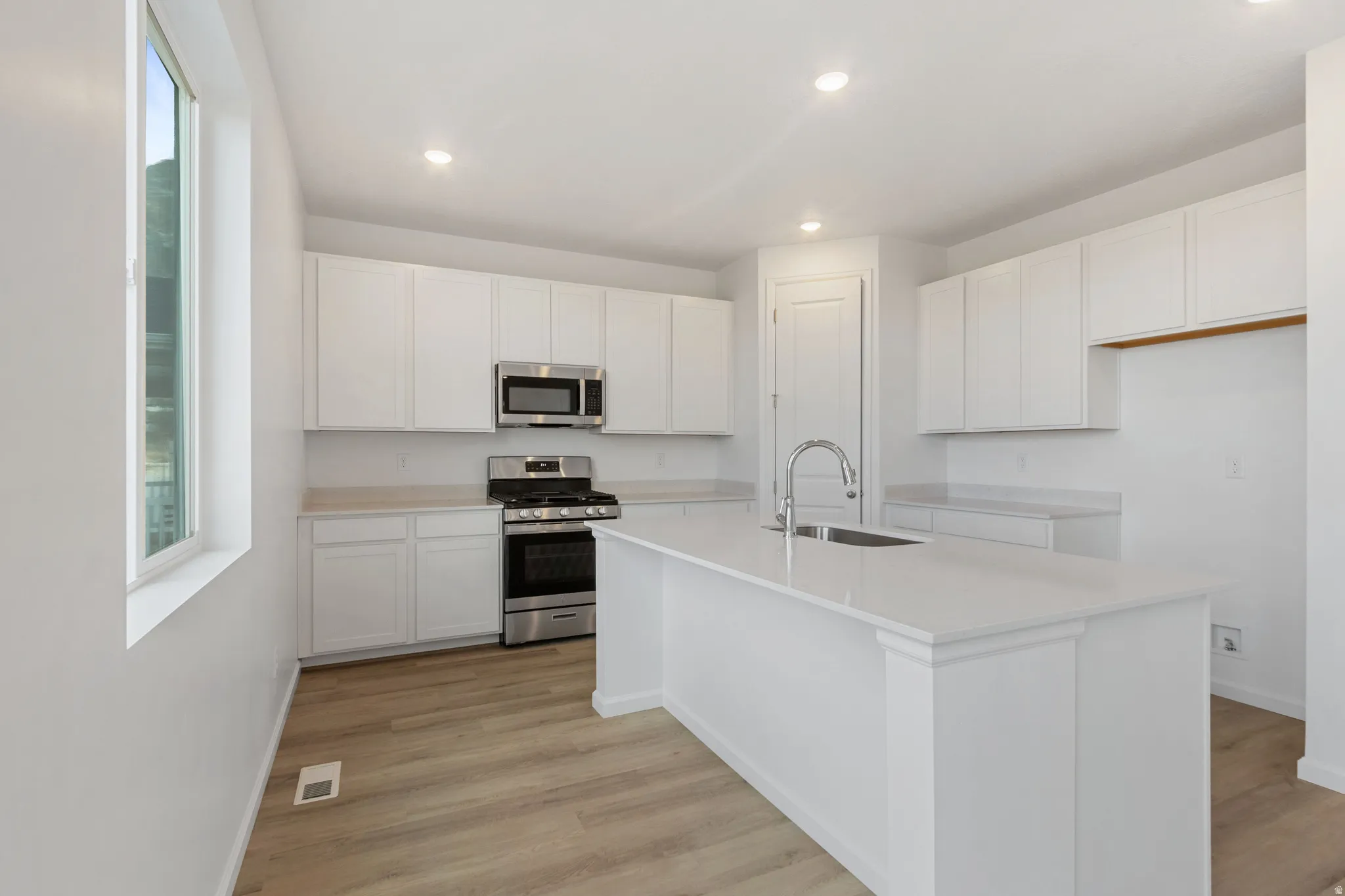 Kitchen featuring white cabinetry, stainless steel appliances, light wood finished floors, a kitchen island with sink, and recessed lighting