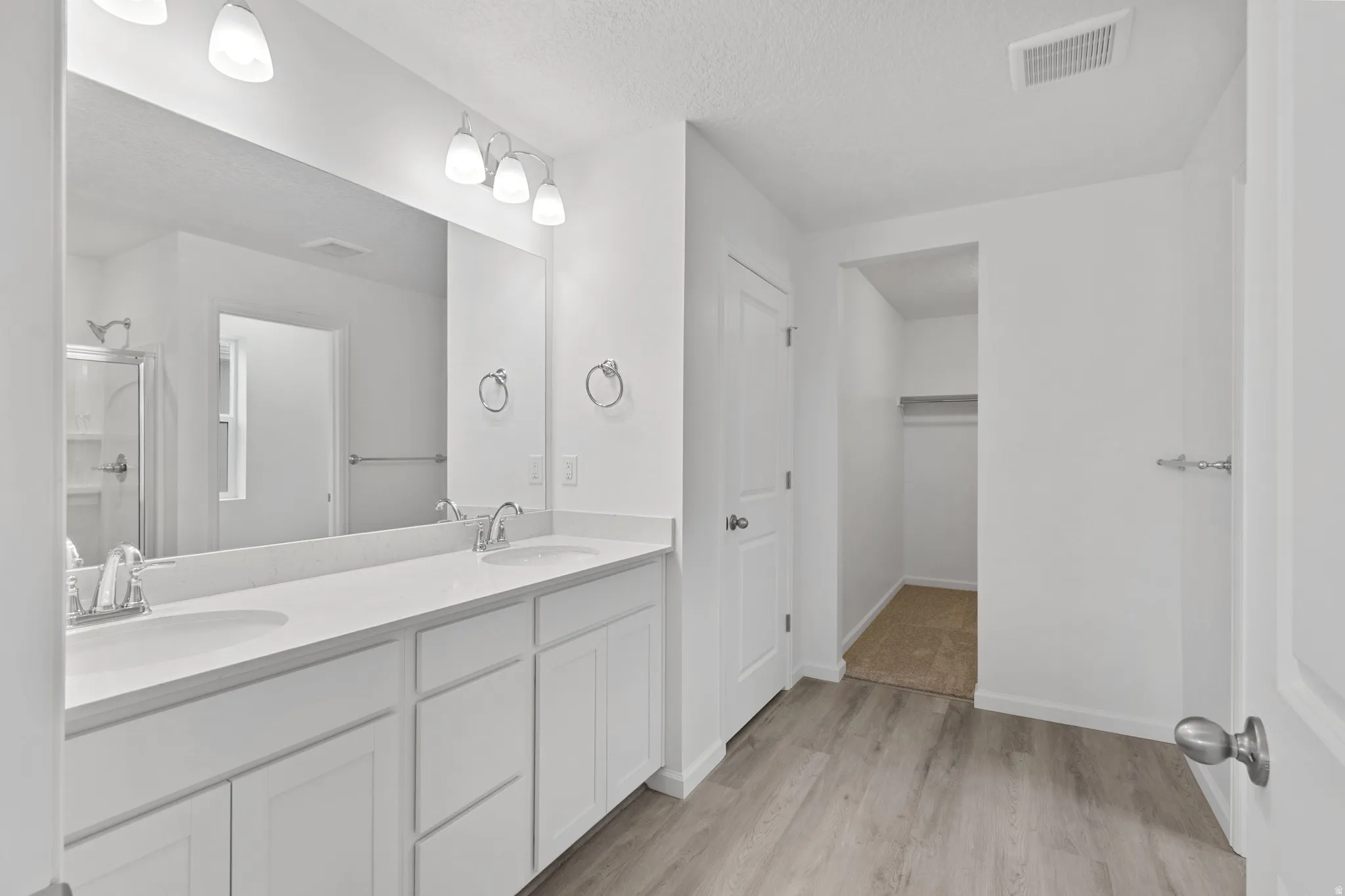 Full bath featuring double vanity, light wood finished floors, a textured ceiling, a shower stall, and a spacious closet