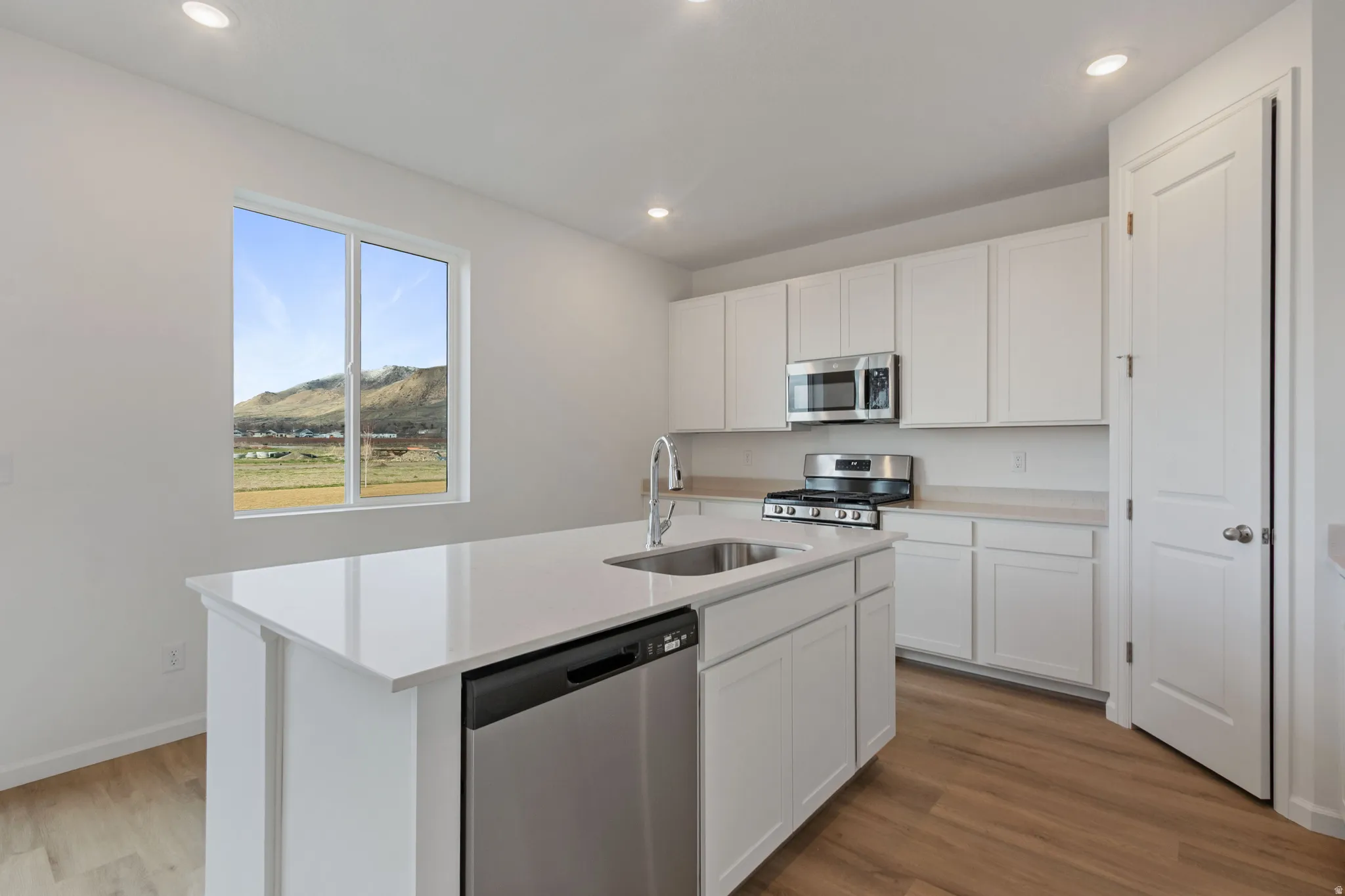 Kitchen with stainless steel appliances, white cabinets, light wood-type flooring, and recessed lighting