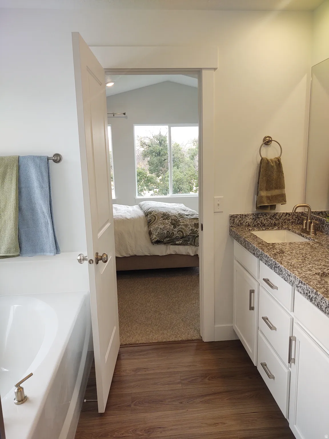 Ensuite bathroom with double vanity, a garden tub, and dark wood finished floors