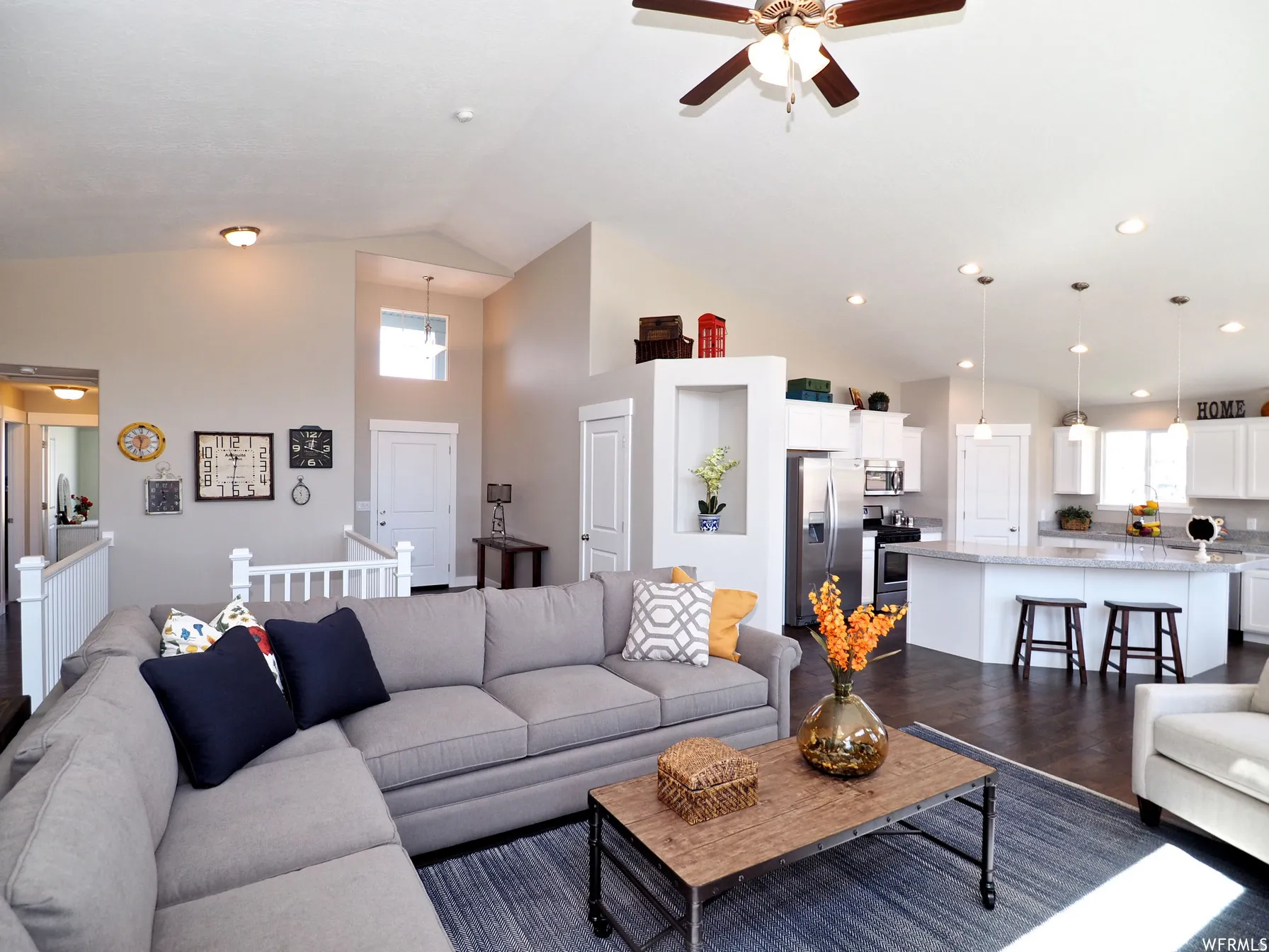 Living room with dark wood-type flooring, vaulted ceiling, ceiling fan, and healthy amount of natural light
