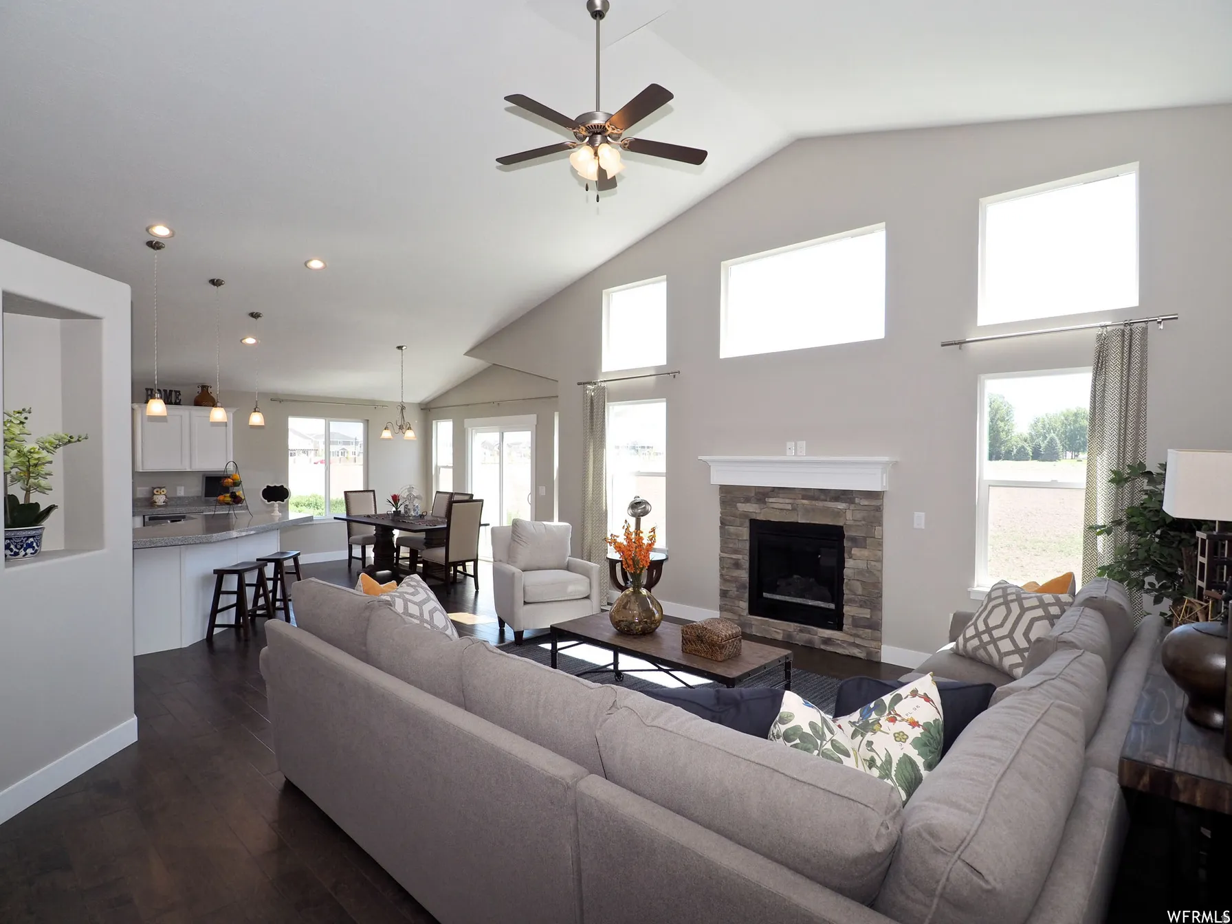 Living area featuring a ceiling fan, dark wood-type flooring, a fireplace, vaulted ceiling, and suspended lighting