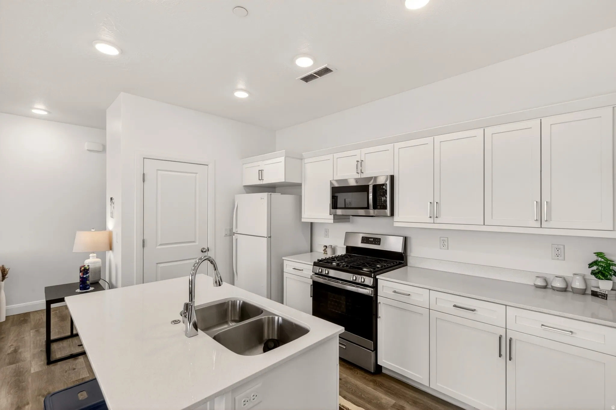 Kitchen with stainless steel appliances, dark wood finished floors, white cabinetry, an island with sink, and light stone counters