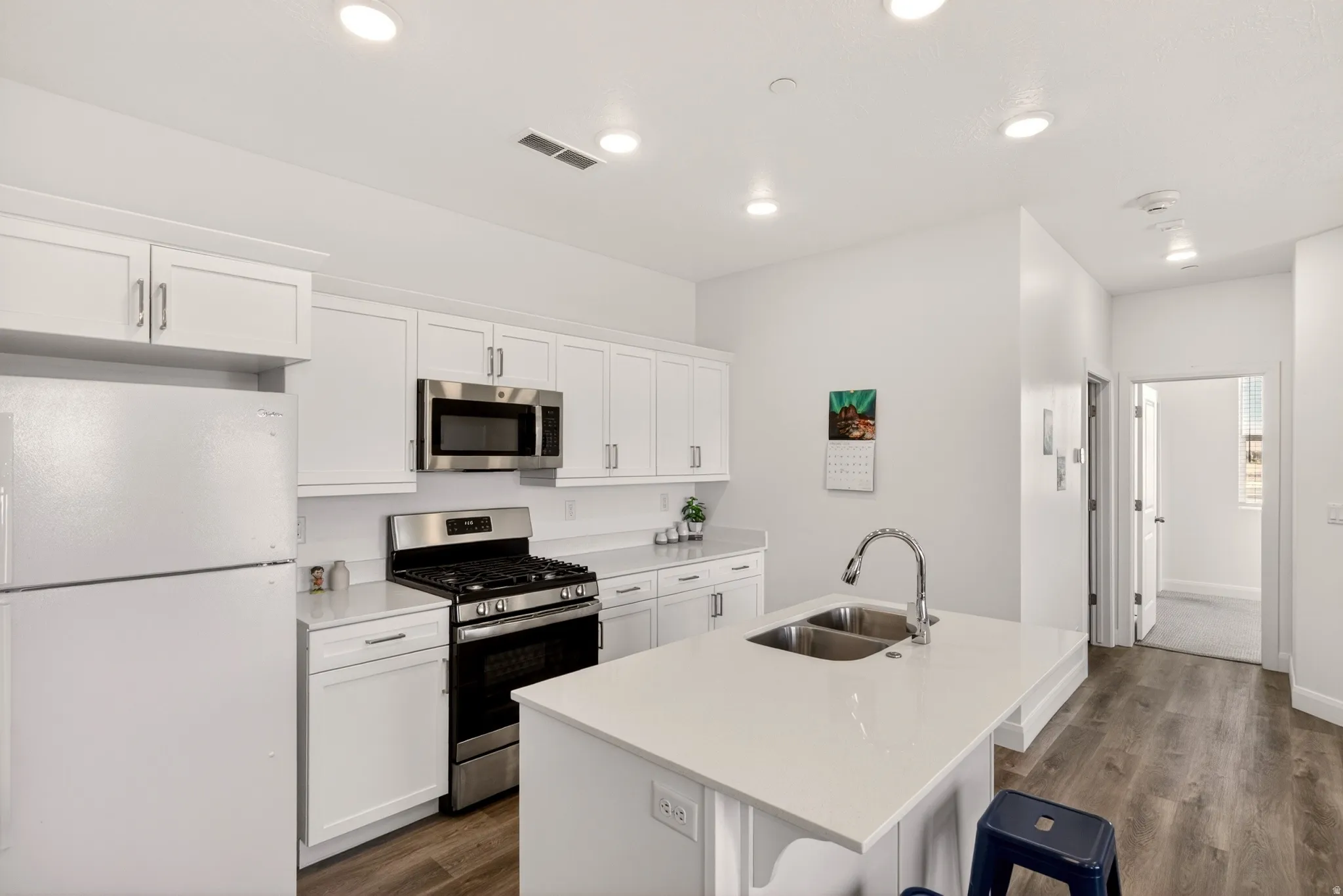 Kitchen with stainless steel appliances, white cabinetry, a center island with sink, dark wood-type flooring, and recessed lighting