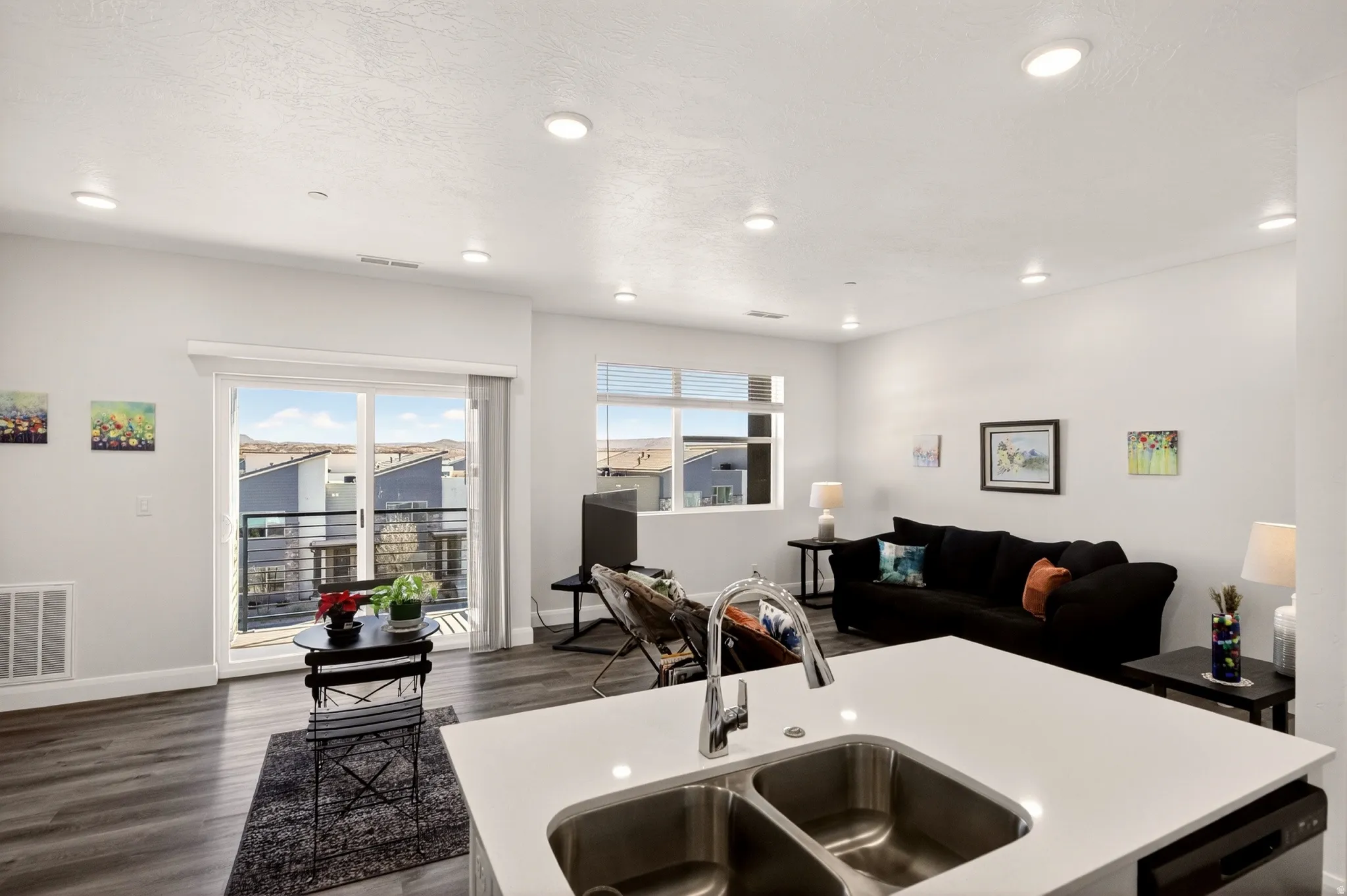 Kitchen featuring dark wood finished floors, open floor plan, light countertops, a kitchen island with sink, and stainless steel dishwasher