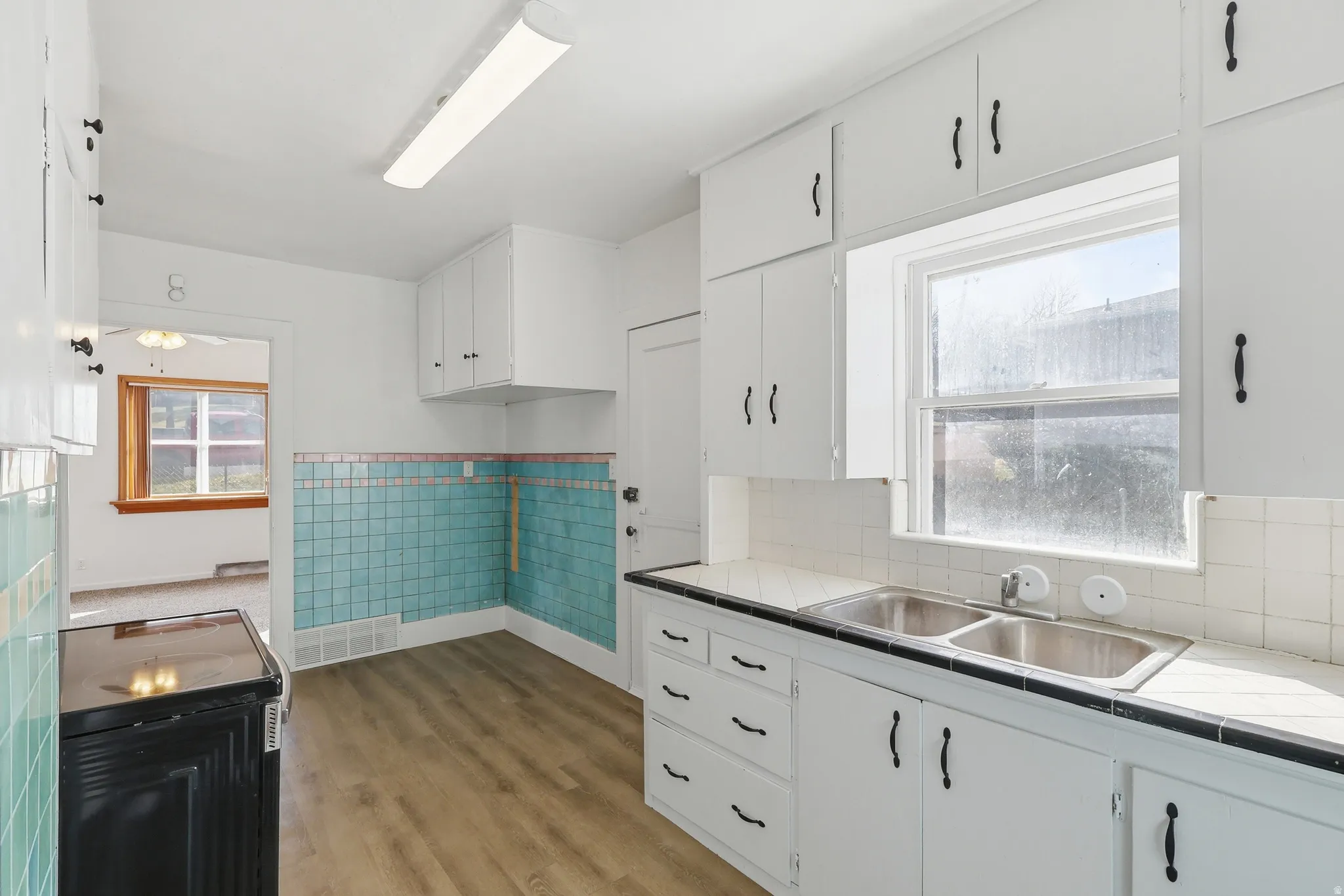 Kitchen featuring white cabinets, black electric range, tile counters, a wainscoted wall, and light wood-type flooring